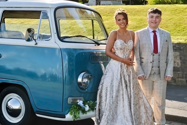 Couple in prom outfits beside the blue and cream VW camper prom car in Lancashire